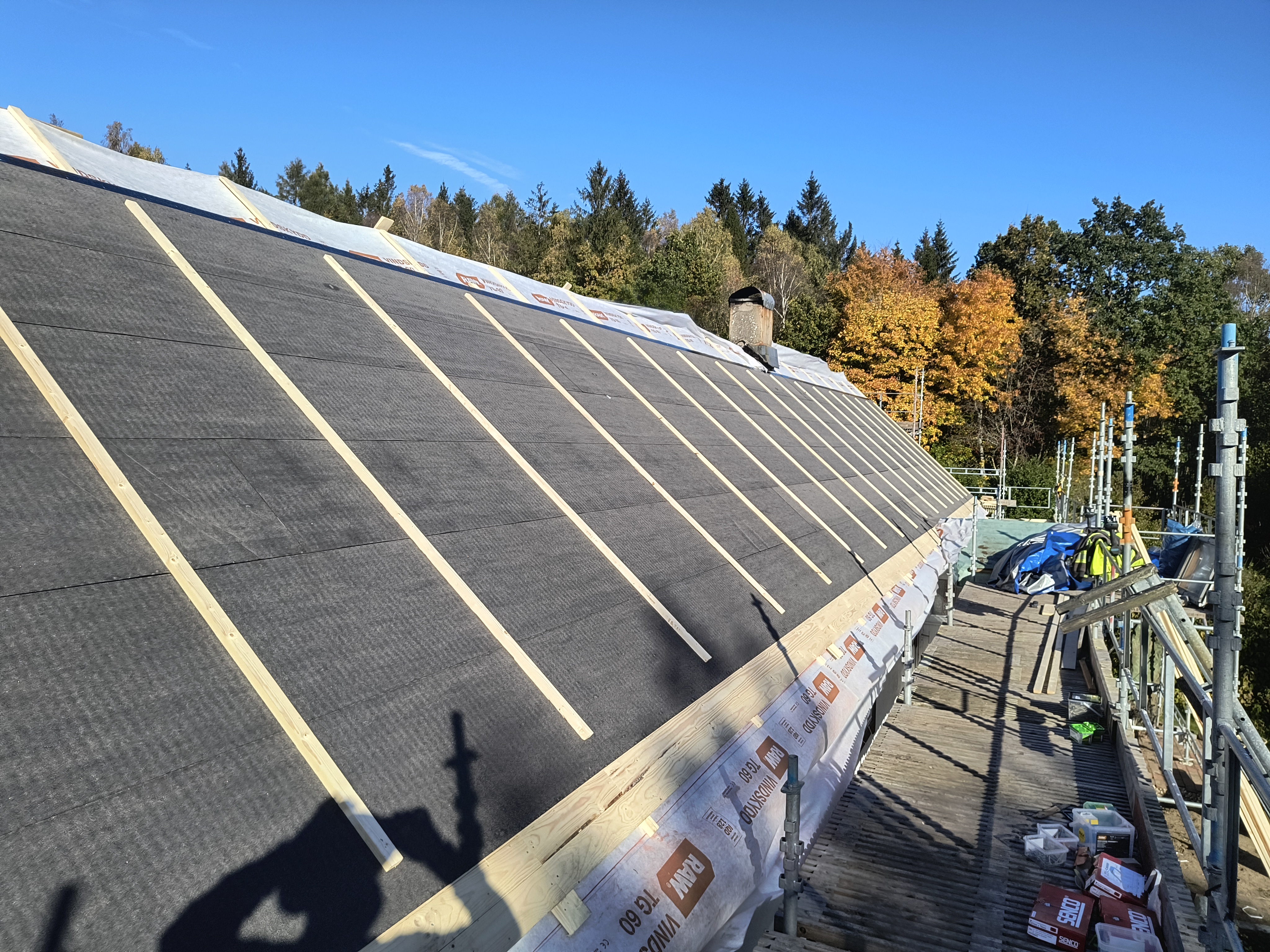 Takomläggning på en villa där nytt, tätt underlag med råspont och takpapp är lagt, även runt en stor tak-kupa. Taket är nu förberett för montering av ett nytt plåttak.