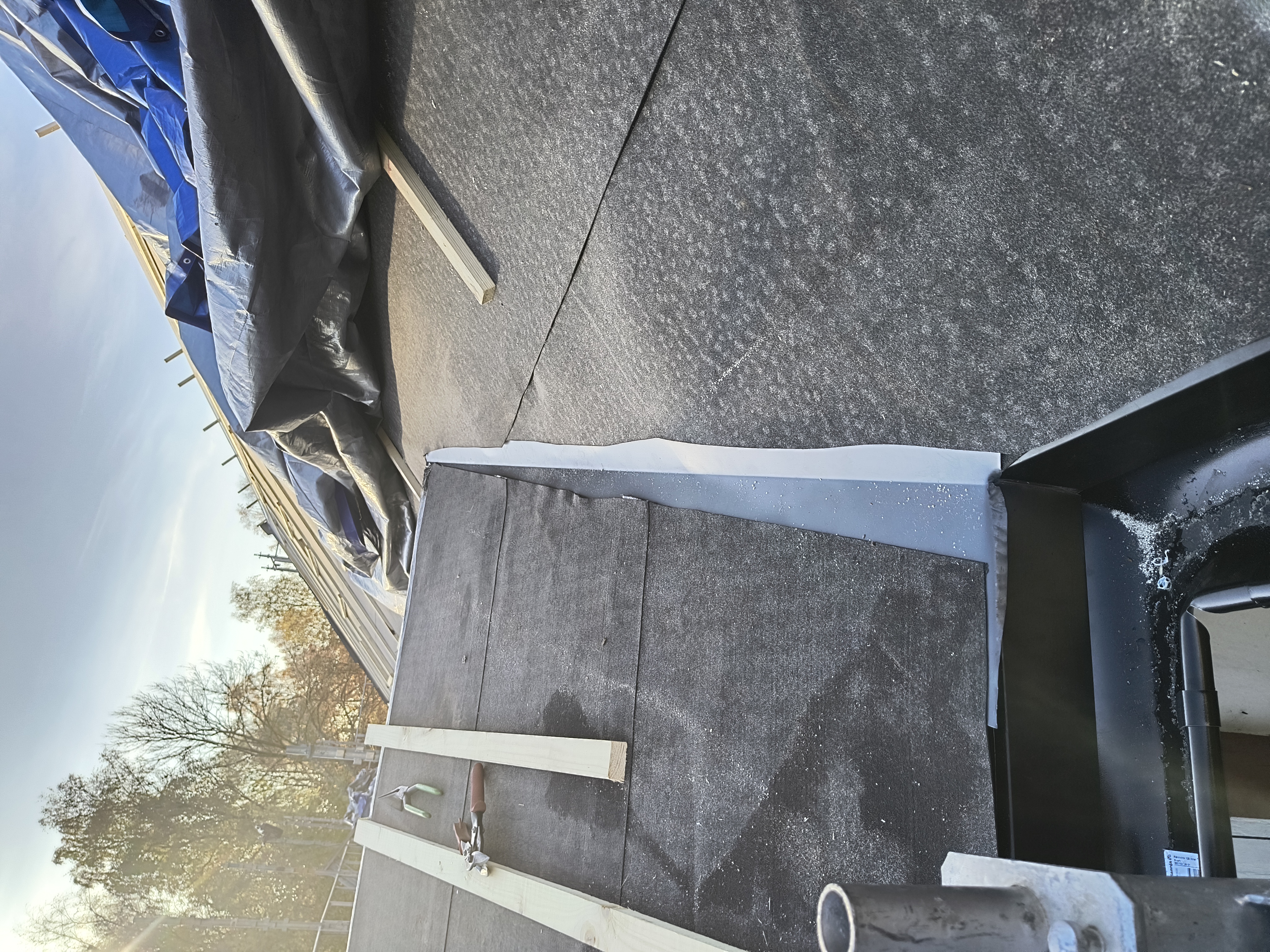 Takomläggning på en villa där nytt, tätt underlag med råspont och takpapp är lagt. Taket är nu förberett för montering av ett nytt tak.