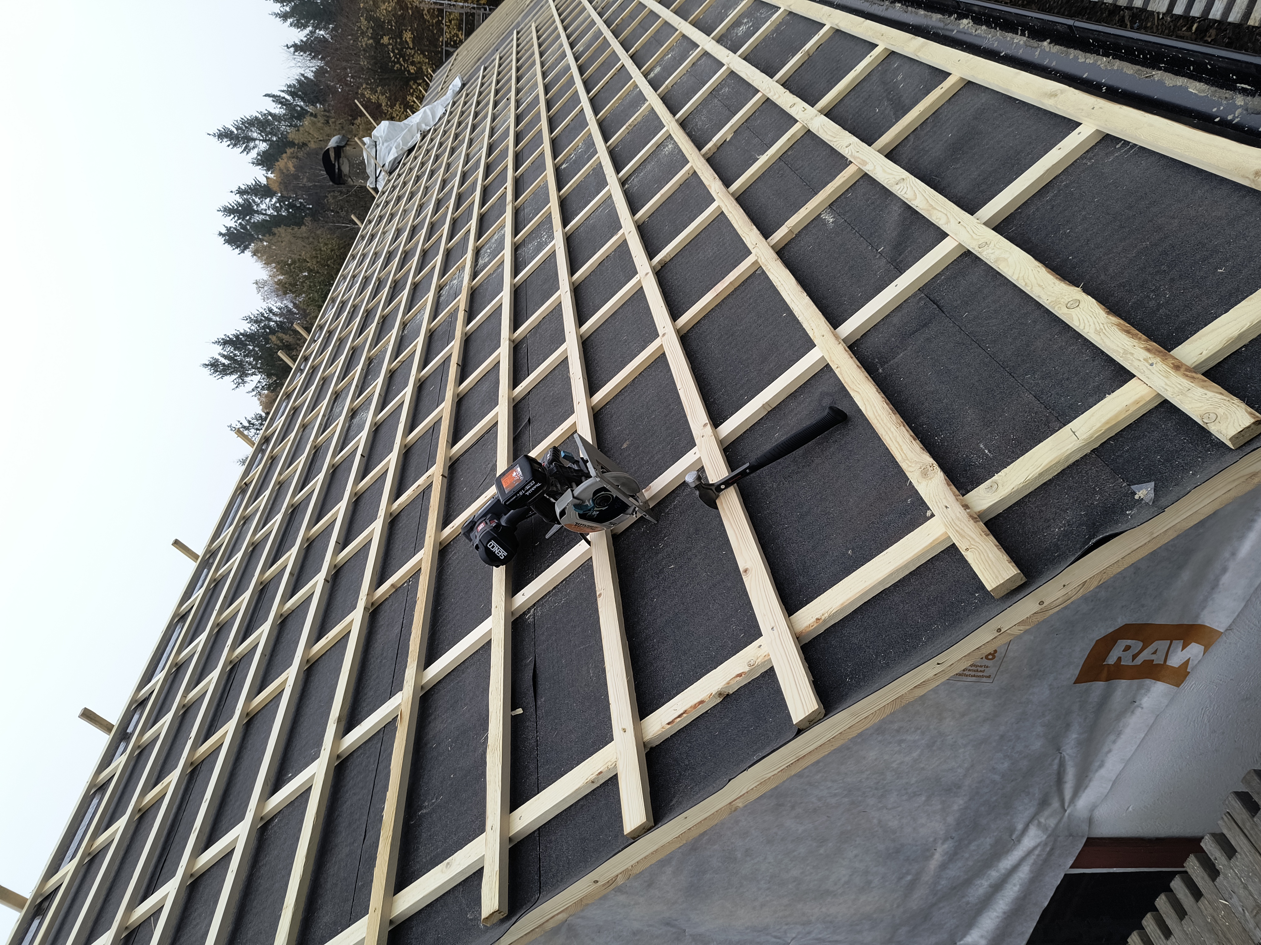 Takomläggning på en villa där nytt, tätt underlag med råspont och takpapp är lagt. Taket är nu förberett för montering av ett nytt tak.